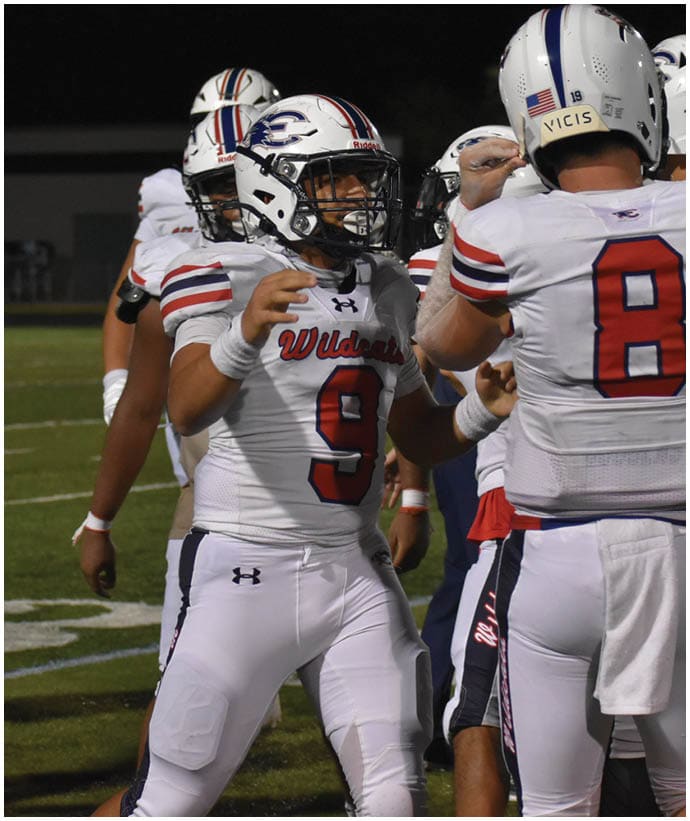 People in football uniforms are on a field at night, with one person wearing number 9 and another wearing number 8 engaging in a celebratory gesture. Description generated by AI