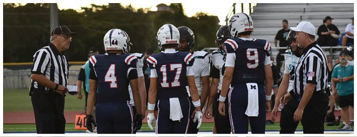 Several people wearing athletic clothing and cleats stand on a sports field with a large logo on the ground beneath them. Description generated by AI