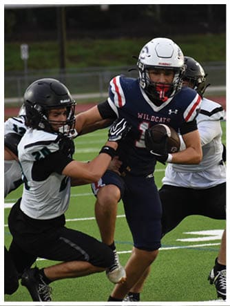 Two people in football uniforms are engaged in a play on a field, with one player attempting to tackle the other who is holding the ball. Description generated by AI