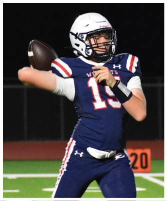 A person wearing a football uniform and helmet is preparing to throw a football on a lit field during a nighttime game. Description generated by AI