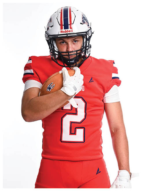 A person wearing a red football uniform and white helmet is holding a football close to their chest while looking forward. Description generated by AI