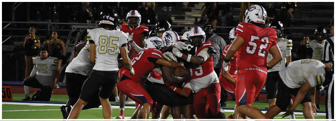 A group of people in football uniforms are engaged in a play on a field with a scoreboard in the background showing the score and time remaining. Description generated by AI
