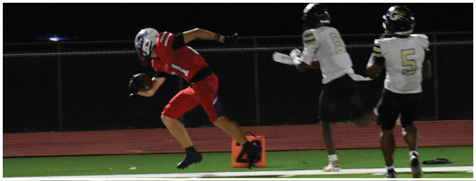 People wearing football uniforms are actively engaged in a game on a grassy field under stadium lights. Description generated by AI