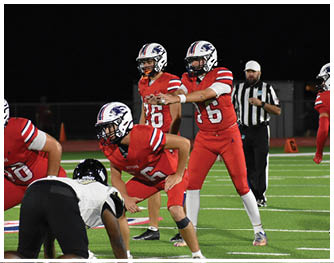 A group of people wearing white football uniforms with helmets are walking on a football field under stadium lights. Description generated by AI