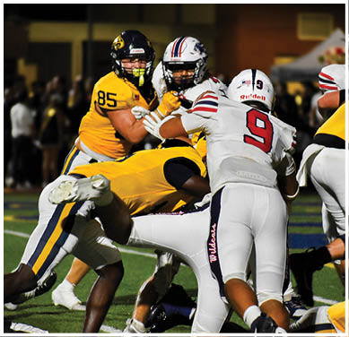 Several football players in yellow and white uniforms are engaged in a play on a field under stadium lights. Description generated by AI