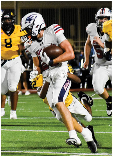 A person in a white football uniform is running with the ball while being pursued by several people in yellow and white football uniforms on a lit field at night. Description generated by AI