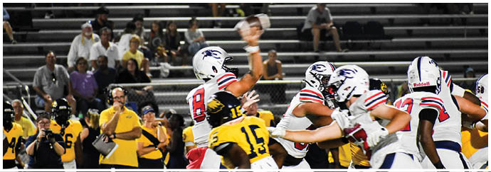 A group of people in football uniforms are engaged in a game on a field with empty bleachers and spectators in the background. Description generated by AI