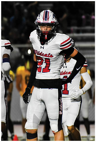 People wearing white football uniforms with red and black accents stand on a field during a game. Description generated by AI