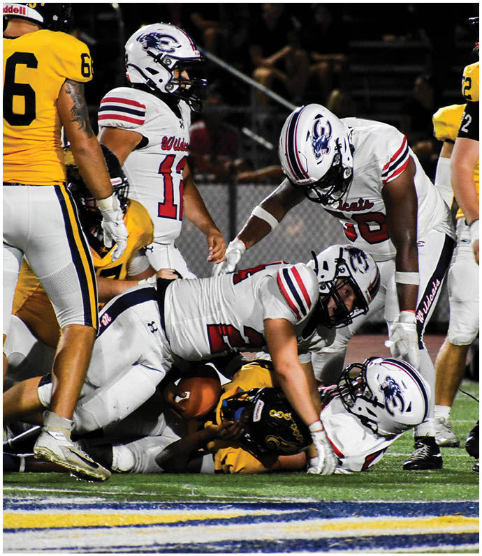 Several football players in white and yellow uniforms are engaged in a tackle on a field during a game. Description generated by AI