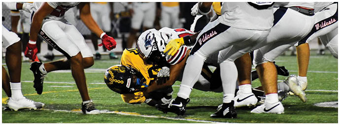 People in football uniforms are engaged in a play on a field with one person in yellow being tackled by several people in white uniforms. Description generated by AI