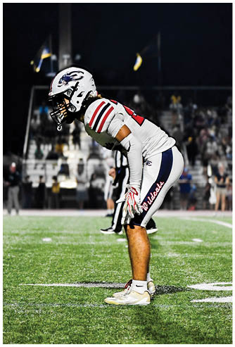 A person in a white sports uniform with red and black stripes is bending forward on a field at night with a blurred background. Description generated by AI