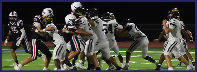 People in football uniforms are engaged in a play on a well-lit field at night. Description generated by AI