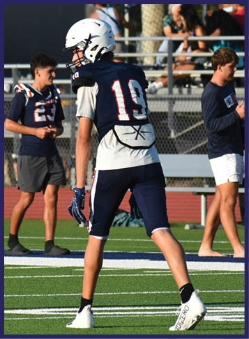 Two people in football uniforms are on a field at night with one person running while holding the ball and the other reaching to tackle them. Description generated by AI