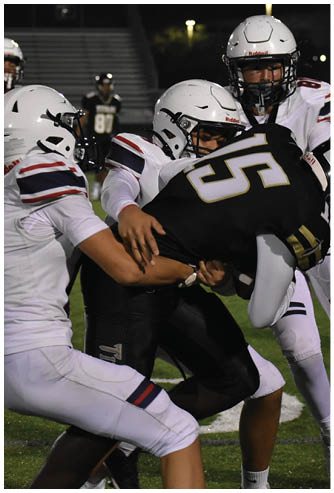 Two people wearing football uniforms and helmets are engaged in a tackle during a game on a grassy field. Description generated by AI