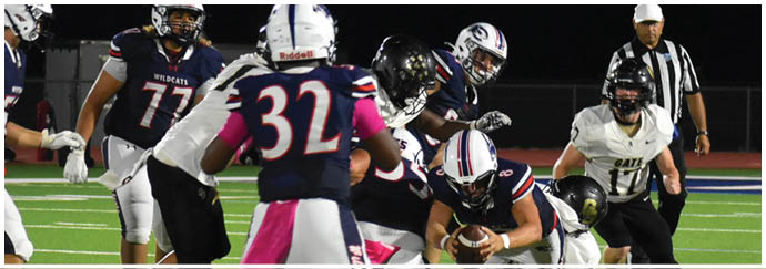 People in football uniforms are engaged in a play on a well-lit field with one person holding the ball while others are either tackling or running. Description generated by AI