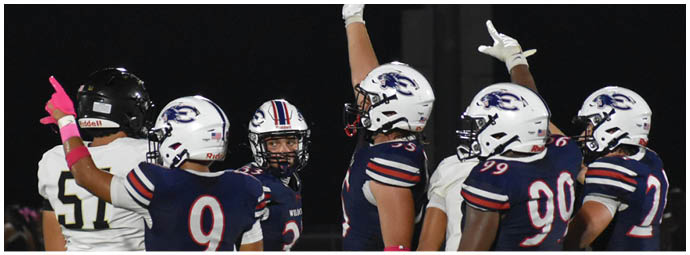Several people wearing football uniforms are standing together on a field with artificial turf and yard lines. Description generated by AI