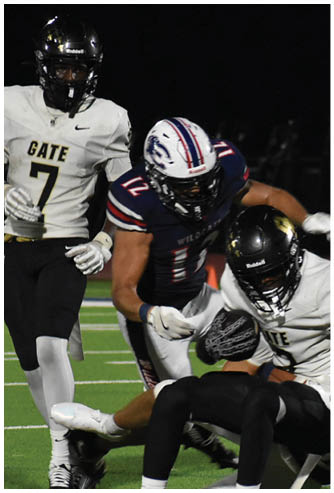A group of people in football uniforms are actively engaged in a tackle on a green field during a game. Description generated by AI