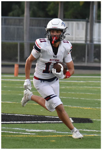 A person wearing a white football uniform and helmet is running on a football field while holding a football. Description generated by AI