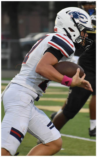 A person wearing a white sports uniform with a pink wristband is holding a football tightly while running on a field. Description generated by AI