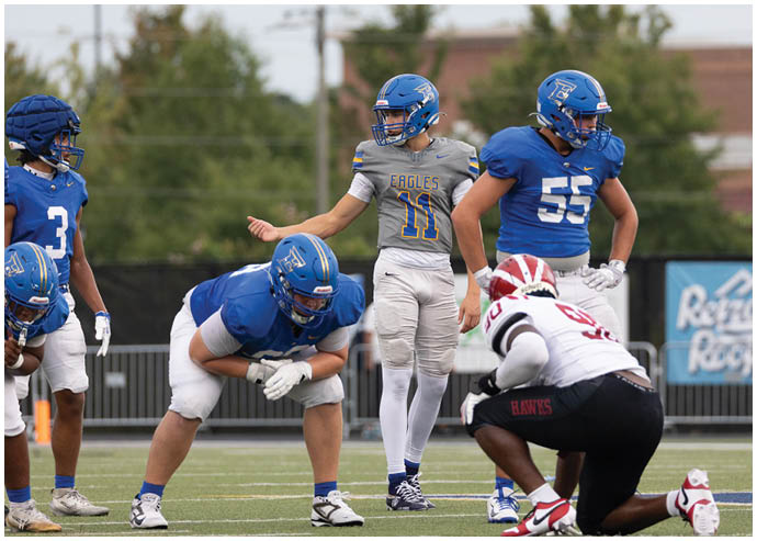 Three football players in blue and white uniforms running on a field. Description generated by AI
