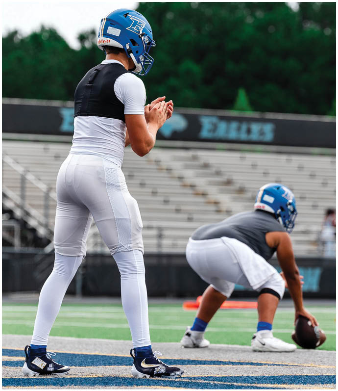 Three football players in blue and white uniforms running on a field. Description generated by AI