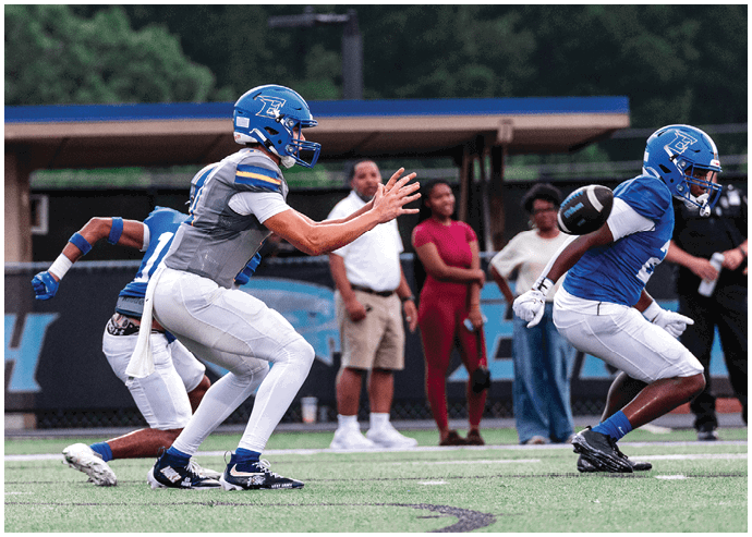 Three football players in blue and white uniforms running on a field. Description generated by AI