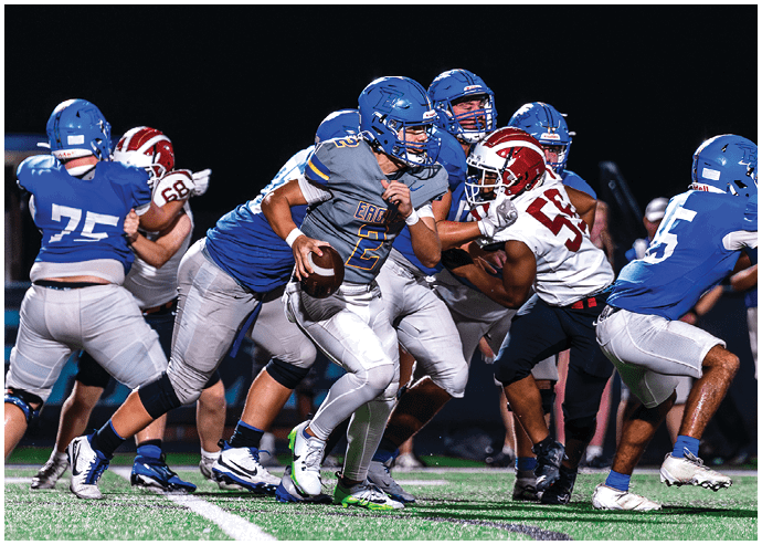 Three football players in blue and white uniforms running on a field. Description generated by AI