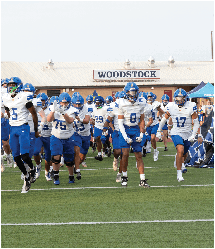 Three football players in blue and white uniforms running on a field. Description generated by AI