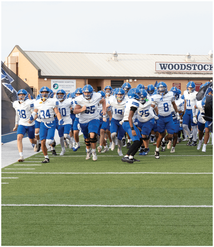Three football players in blue and white uniforms running on a field. Description generated by AI