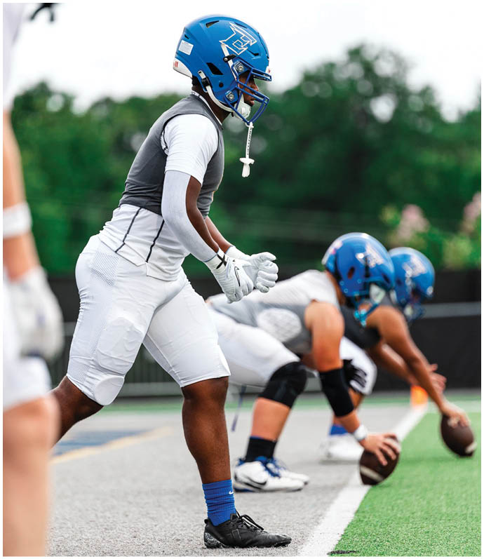 Three football players in blue and white uniforms running on a field. Description generated by AI
