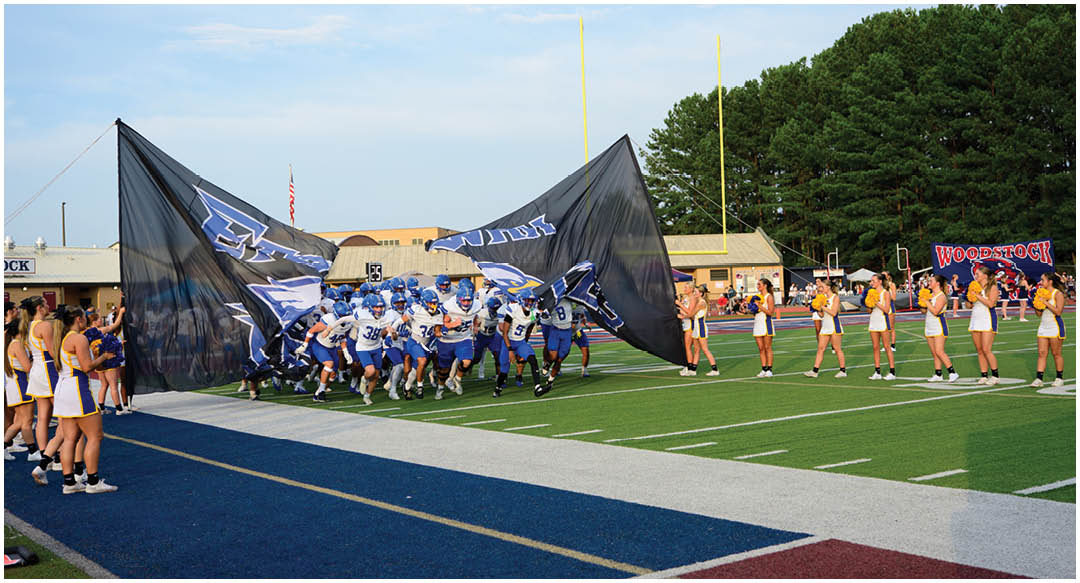 Three football players in blue and white uniforms running on a field. Description generated by AI