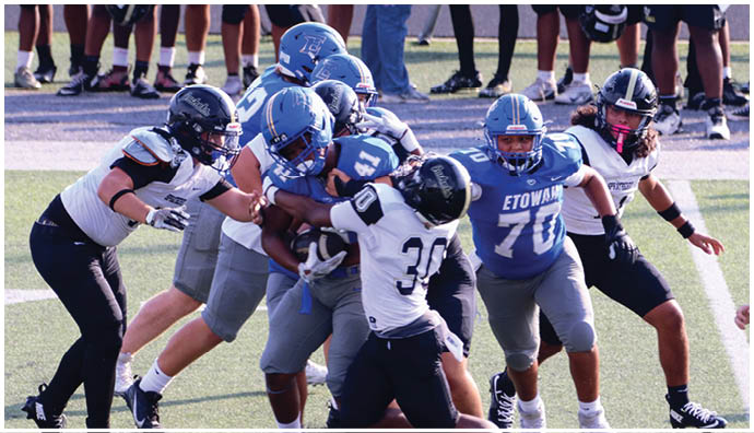 Three football players in blue and white uniforms running on a field. Description generated by AI