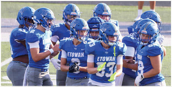 Three football players in blue and white uniforms running on a field. Description generated by AI