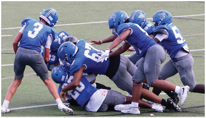 Three football players in blue and white uniforms running on a field. Description generated by AI