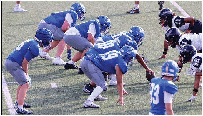 Three football players in blue and white uniforms running on a field. Description generated by AI