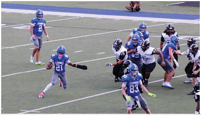 Three football players in blue and white uniforms running on a field. Description generated by AI