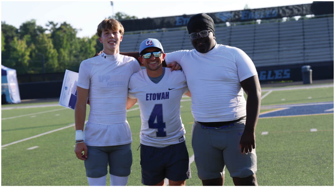 Three football players in blue and white uniforms running on a field. Description generated by AI
