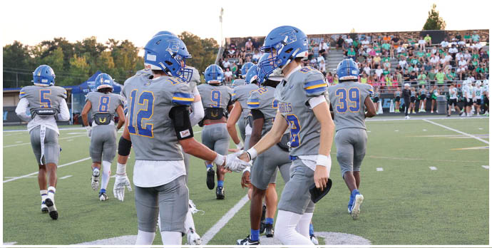 Three football players in blue and white uniforms running on a field. Description generated by AI