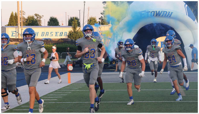 Three football players in blue and white uniforms running on a field. Description generated by AI