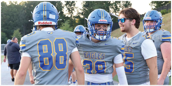 Three football players in blue and white uniforms running on a field. Description generated by AI