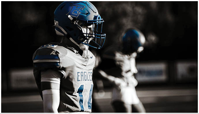Three football players in blue and white uniforms running on a field. Description generated by AI
