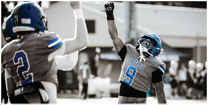 Three football players in blue and white uniforms running on a field. Description generated by AI
