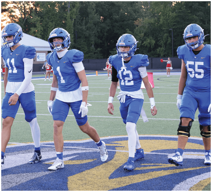 Three football players in blue and white uniforms running on a field. Description generated by AI