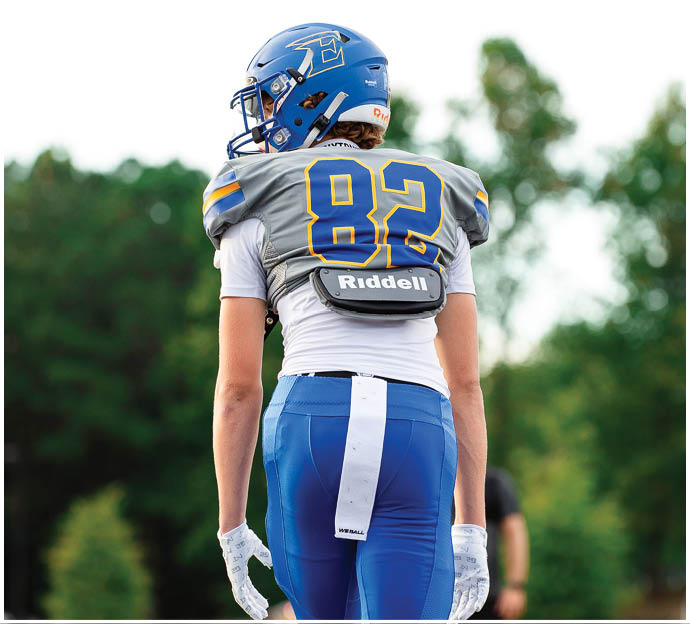Three football players in blue and white uniforms running on a field. Description generated by AI
