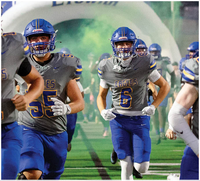 Three football players in blue and white uniforms running on a field. Description generated by AI