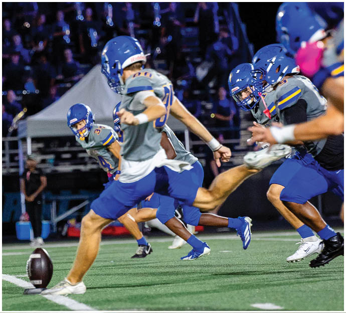 Three football players in blue and white uniforms running on a field. Description generated by AI