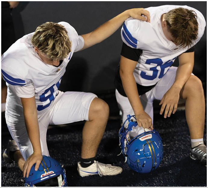 Three football players in blue and white uniforms running on a field. Description generated by AI