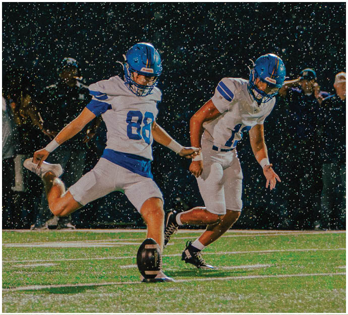 Three football players in blue and white uniforms running on a field. Description generated by AI
