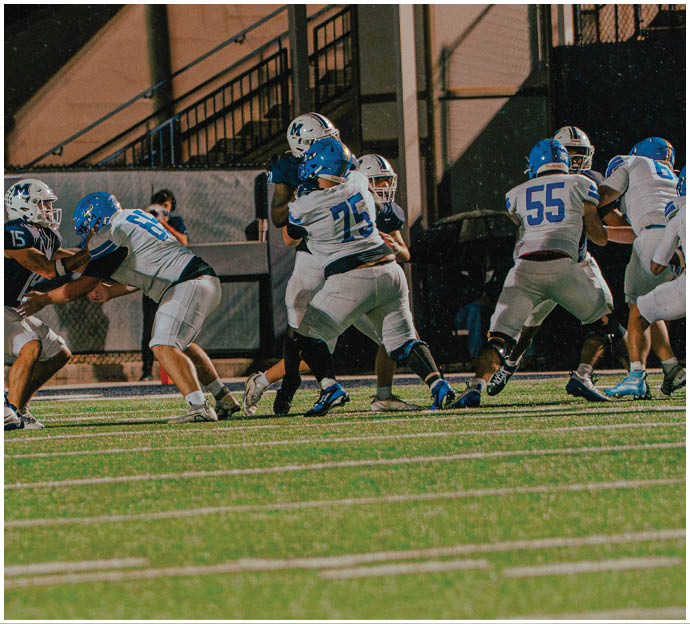 Three football players in blue and white uniforms running on a field. Description generated by AI