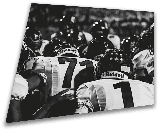 Four people in dark football uniforms and helmets stand in a row on a field, appearing focused and ready for action. Description generated by AI